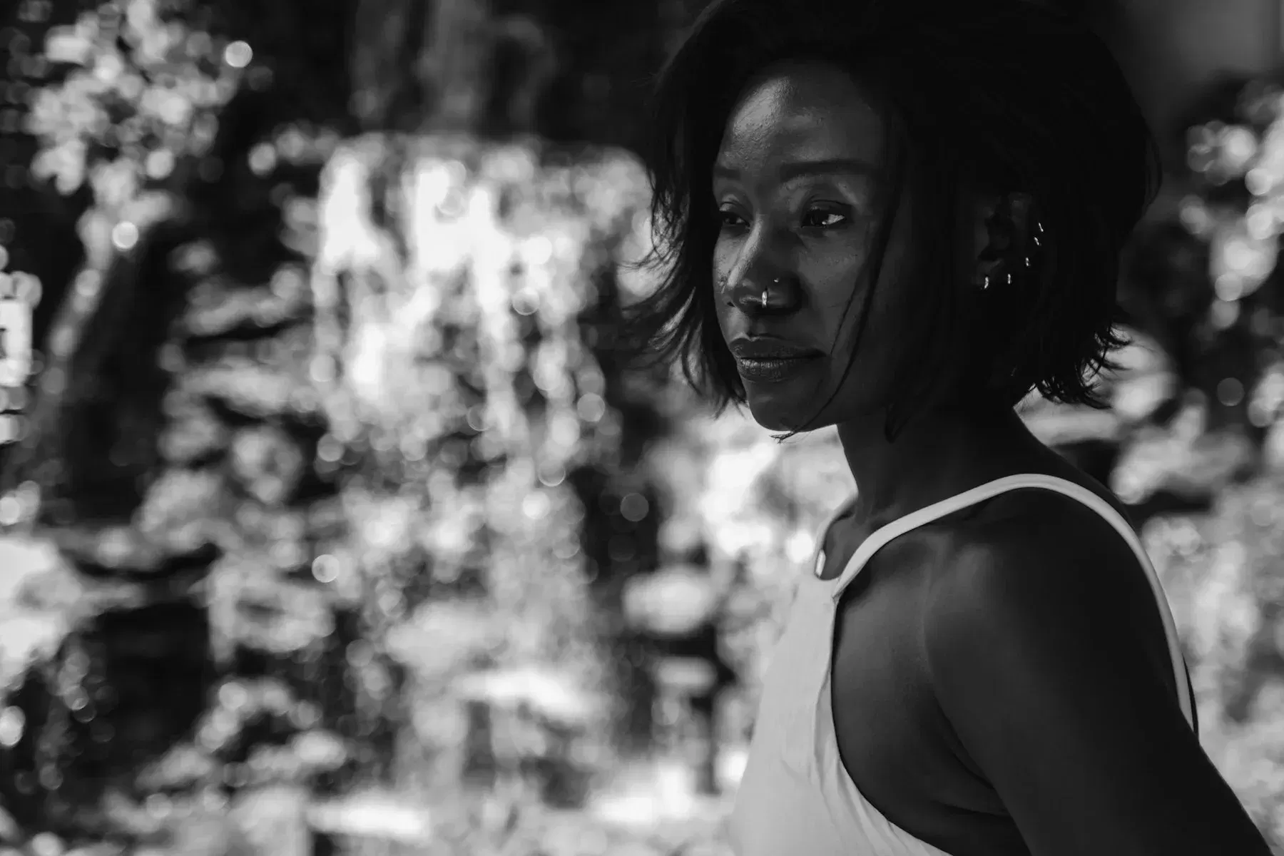 Monochrome portrait of a woman in a white top beneath leafy shadows